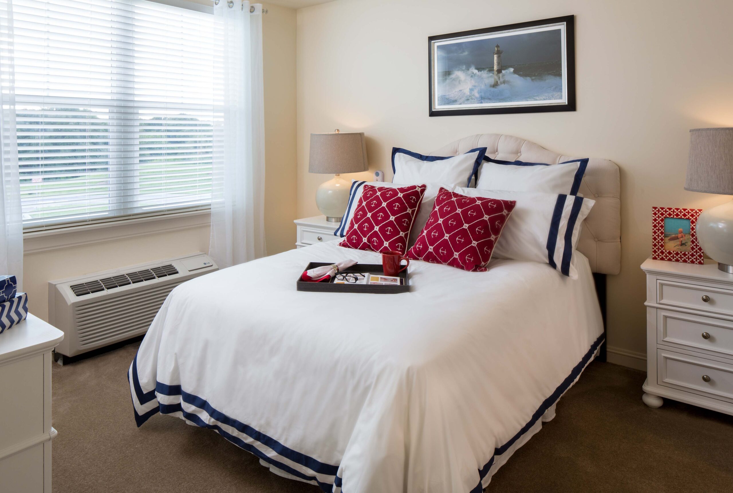 13 - The Summit of Lakewood Ranch A bedroom with white sheets and red throw pillows on it, two lamps on each side of the bed, and a painting at The Summit of Lakewood Ranch.
