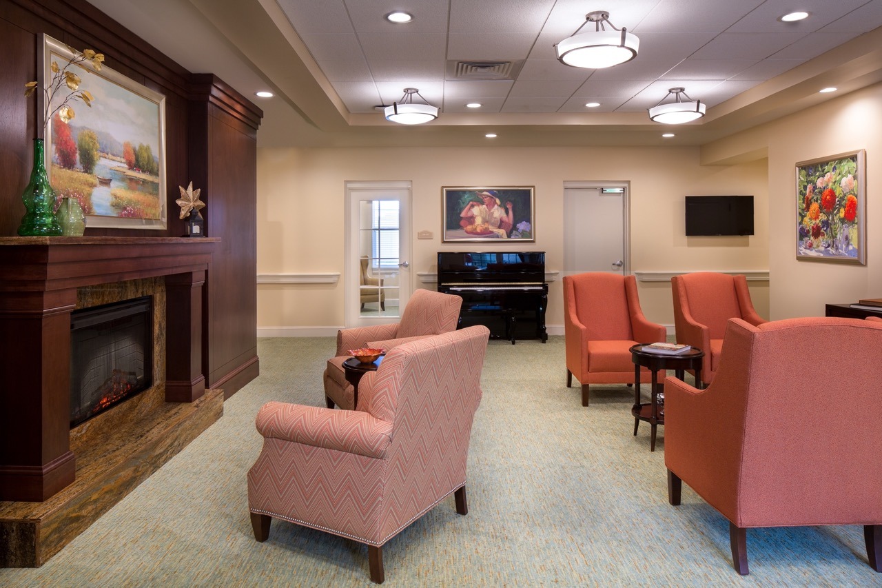 A lobby area with a piano and pink sofa chairs placed in front of the fireplace at The Summit of Lakewood Ranch.